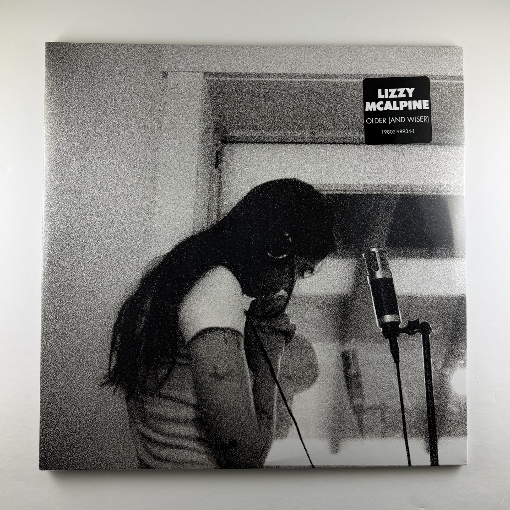 Album cover with a person in front of a microphone, black and white photo style.